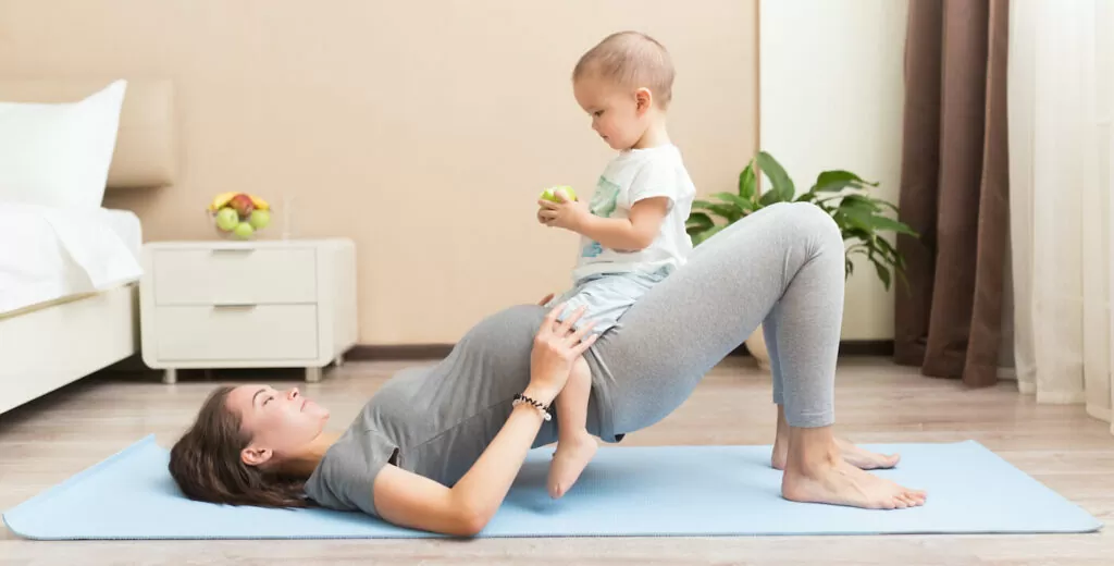 Sportive beautiful pregnant mother with baby son exercising on blue yoga mat. Athletic and healthy motherhood. Fitness, happy maternity and healthy lifestyle concept.